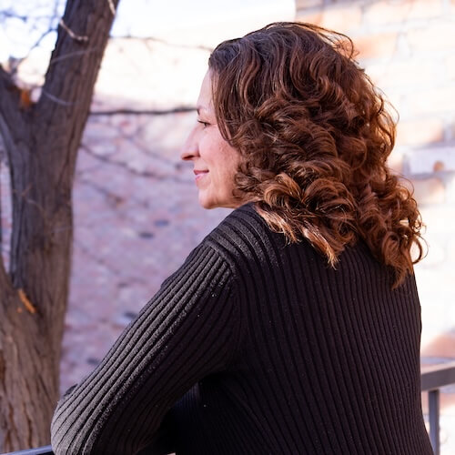 Suzanne muller standing peaceful over a black rod rail looking into the distance side profile
